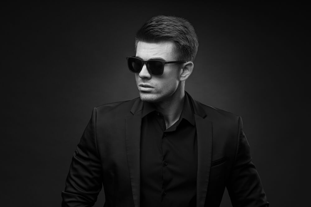 young guy wearing black sunglasses and a black suit